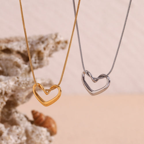 Two heart-shaped necklaces, one gold and one silver, on a beige background.