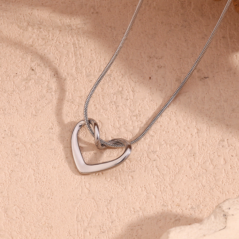 Silver heart-shaped necklace on a beige stone surface