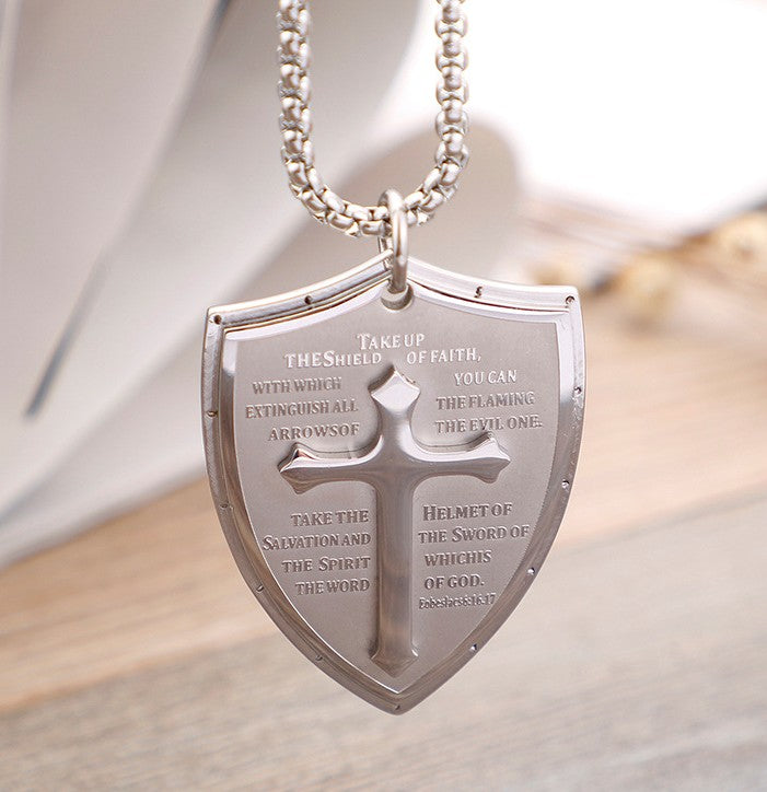 Silver necklace with a shield pendant featuring religious text on a light background