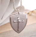 Silver necklace with a shield pendant featuring religious text on a light background