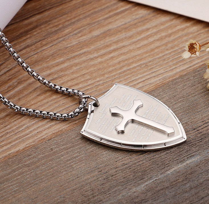 Silver shield-shaped pendant with cross design on a wooden surface