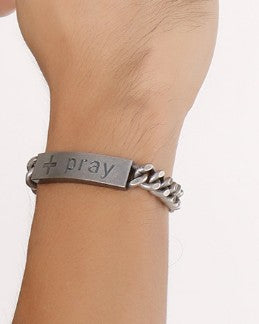 Silver bracelet with 'pray' engraved on a wrist against a white background