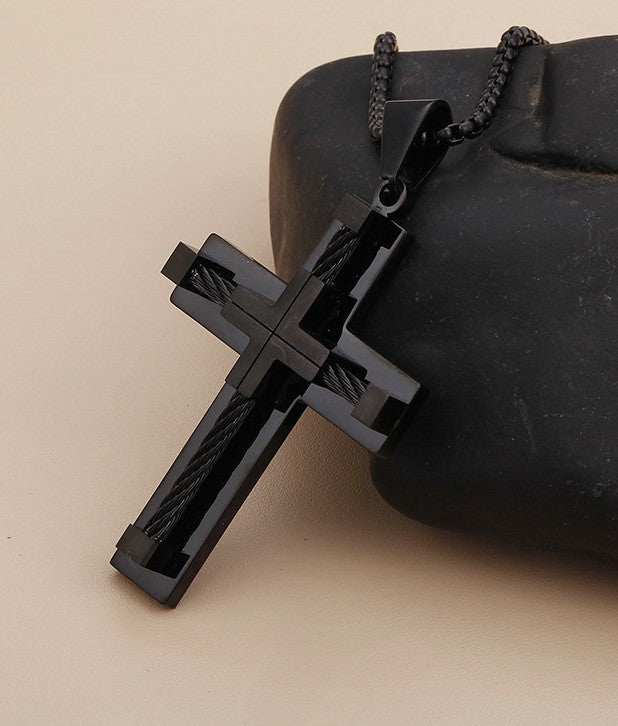 Black cross pendant on a chain against a beige background
