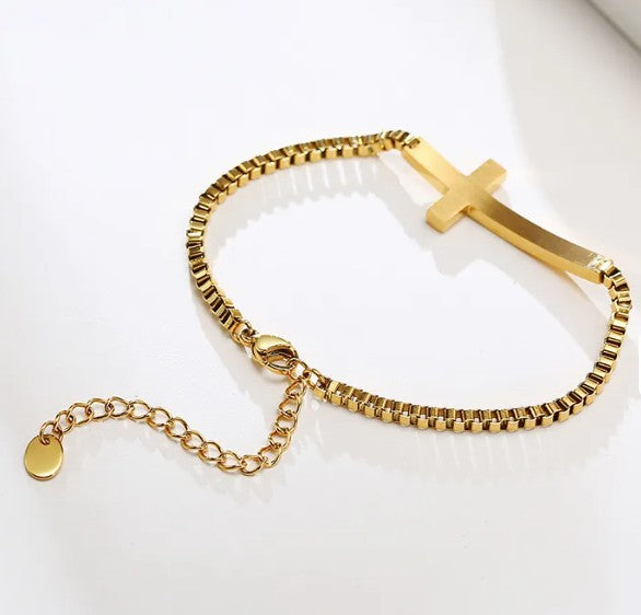 Gold bracelet with a cross charm on a white background