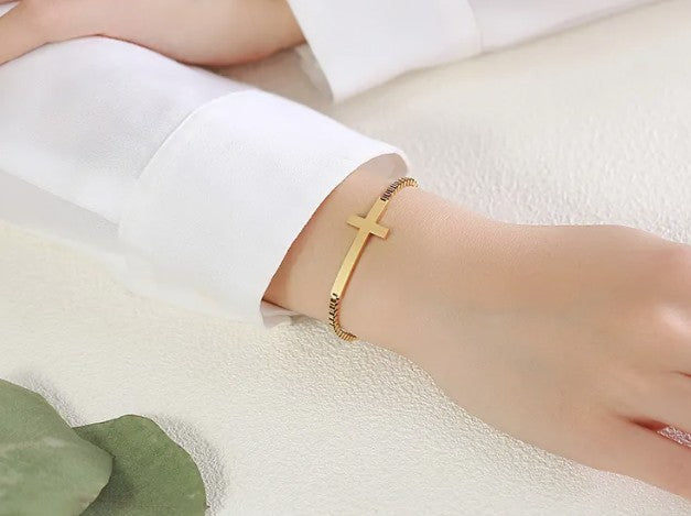 Gold bracelet with a cross design on a wrist against a white background