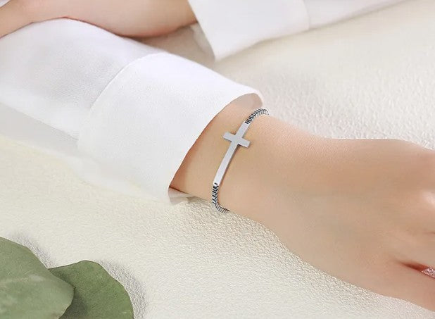 Silver bracelet with a cross design on a person's wrist against a white background