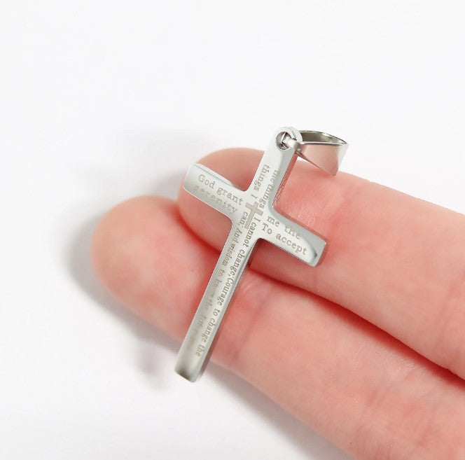 Silver cross pendant held in a hand on a white background