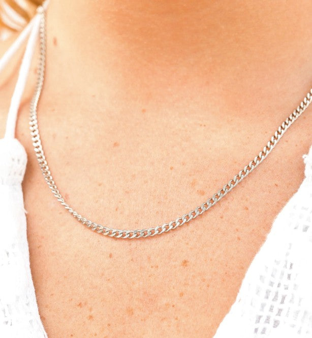 Silver chain necklace on a person's neck with a blurred background