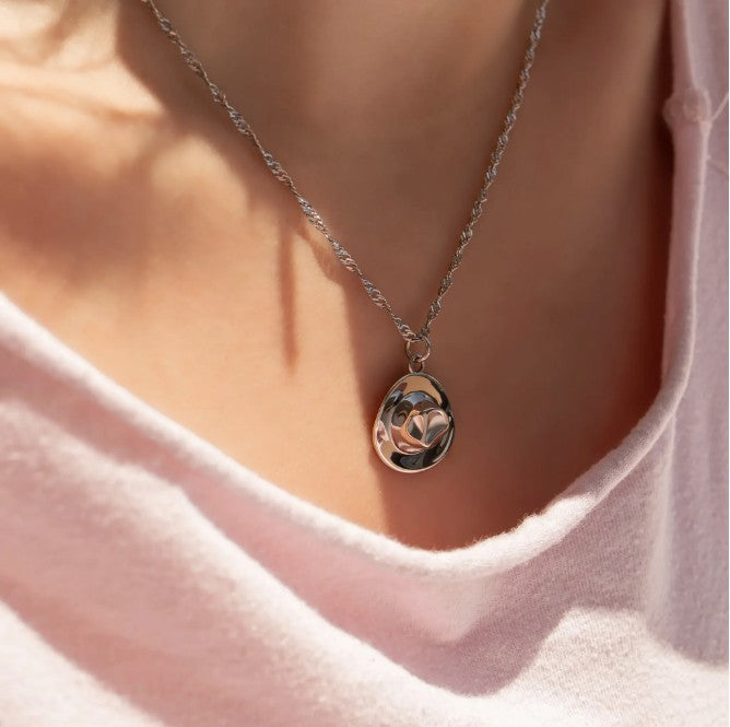 Silver necklace with a pendant worn by a person in a pink shirt