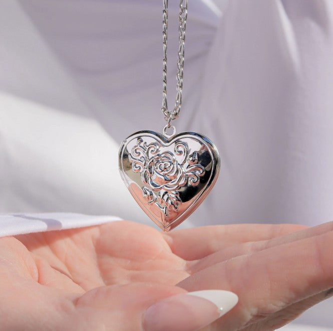 Heart-shaped silver pendant with floral design held in hands against a light background