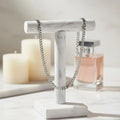 Silver chain on a marble stand with candles and a perfume bottle in the background