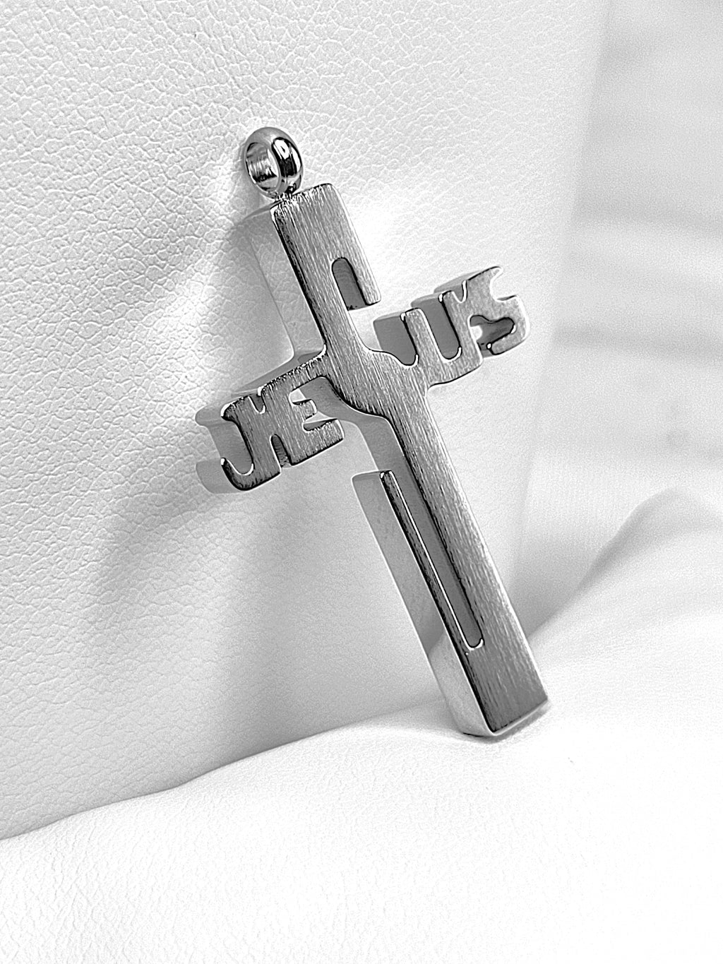 Silver cross pendant with 'Jesus' engraved on a white fabric background