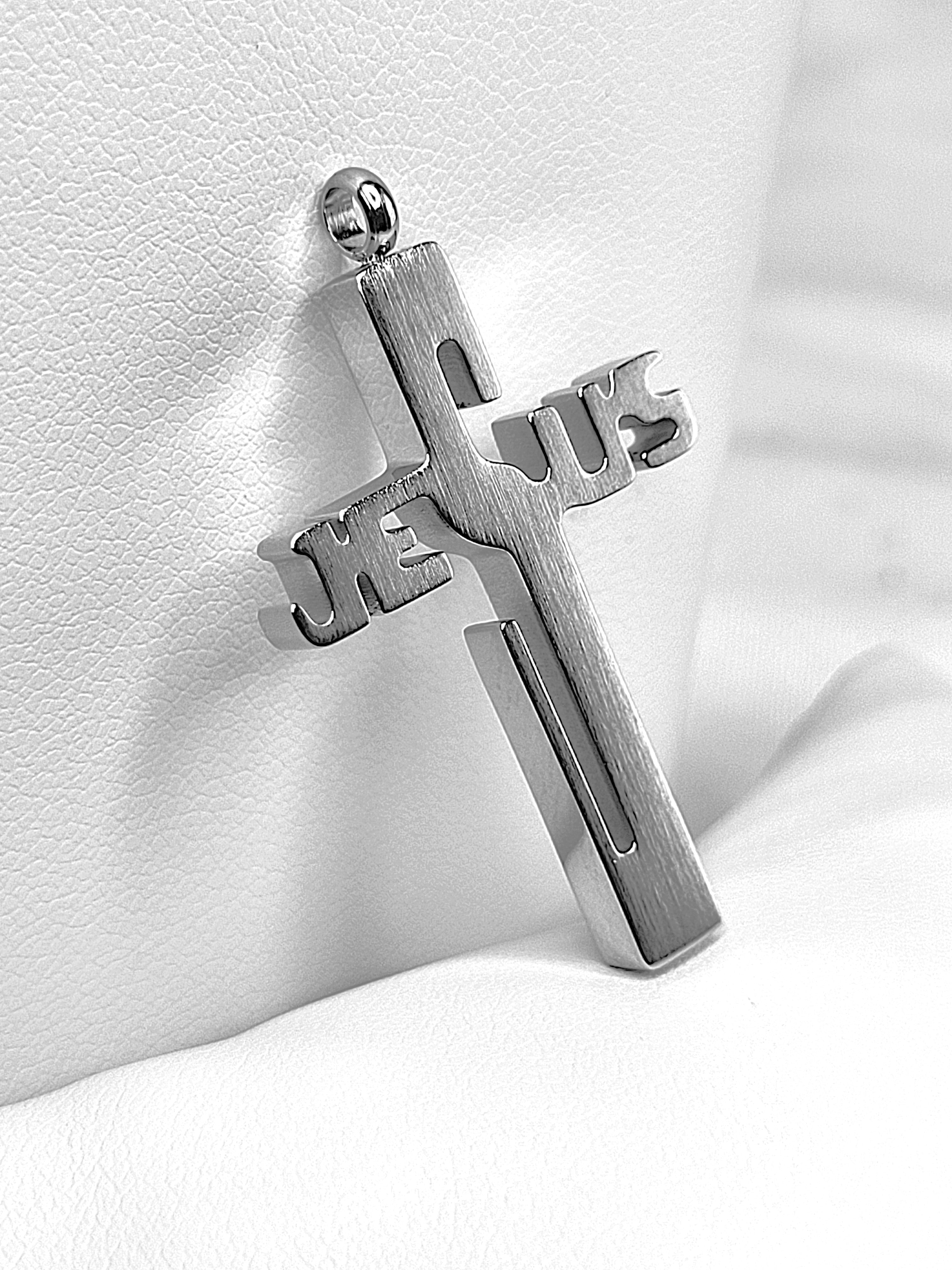 Silver cross pendant with 'Jesus' engraved on a white fabric background