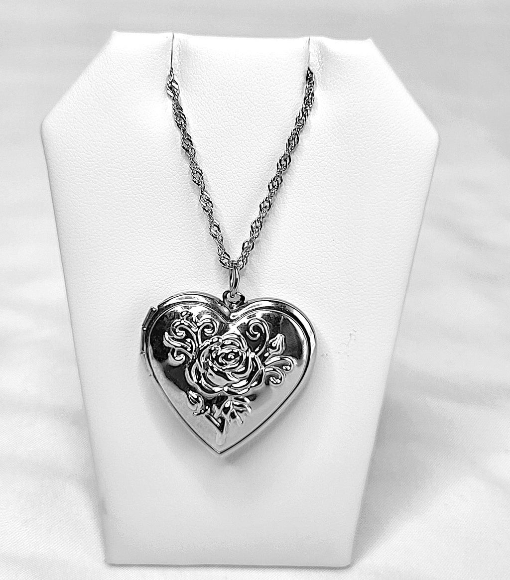 Silver heart-shaped locket with floral design on a white stand