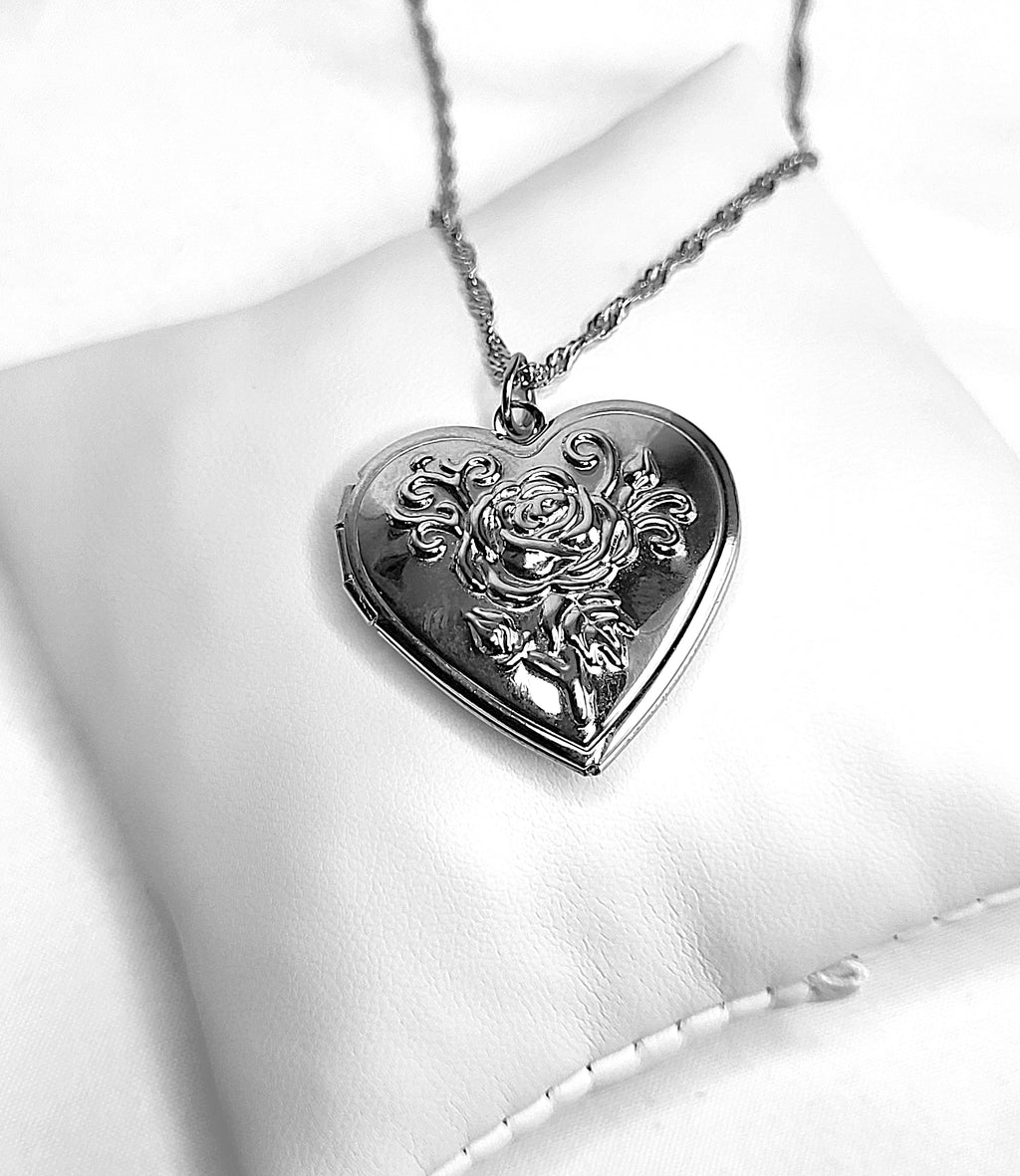 Heart-shaped silver pendant with floral design on a white cushion