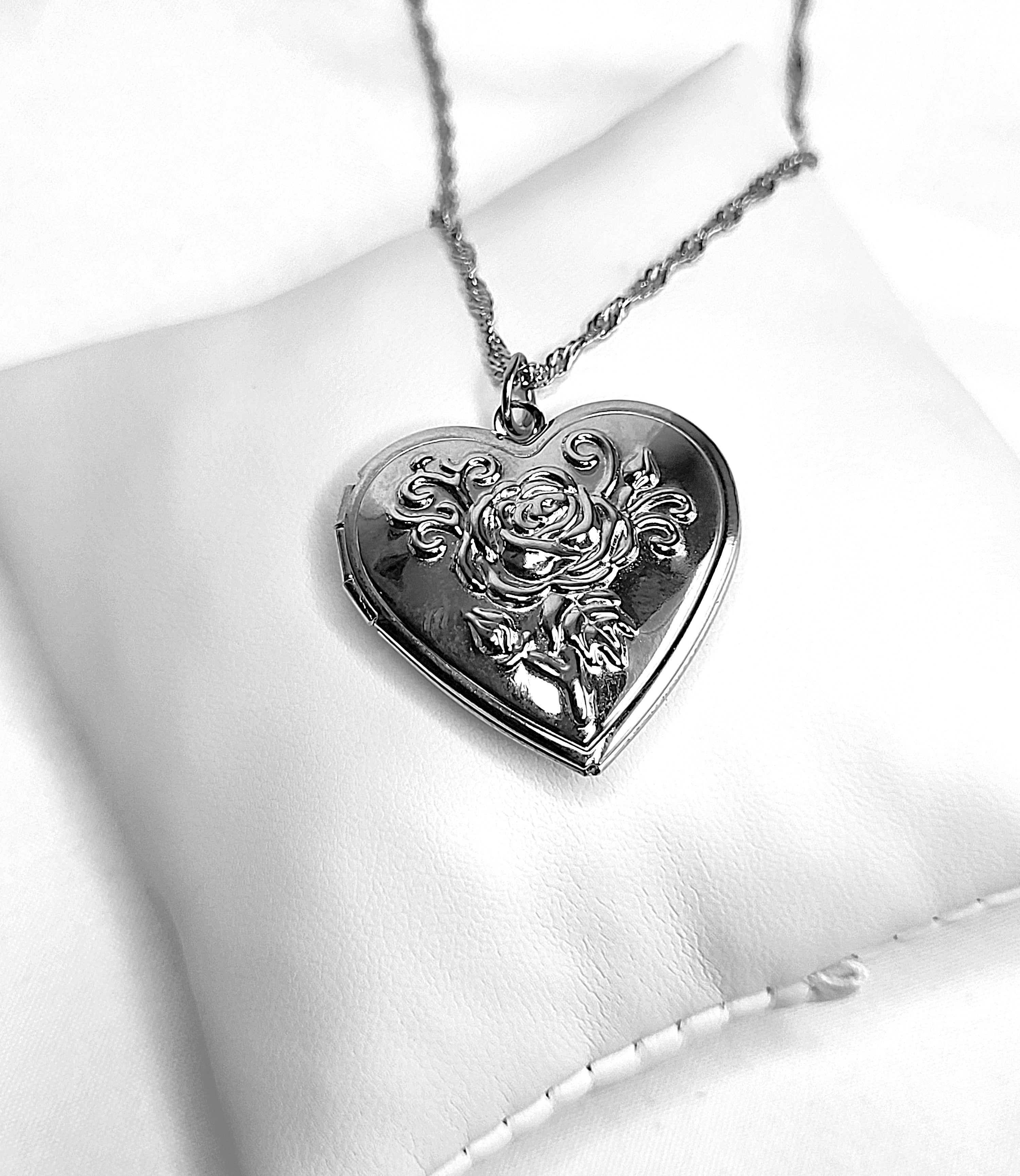 Heart-shaped silver pendant with floral design on a white cushion