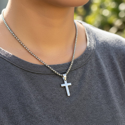 Silver cross pendant on a chain worn by person with great shirt.