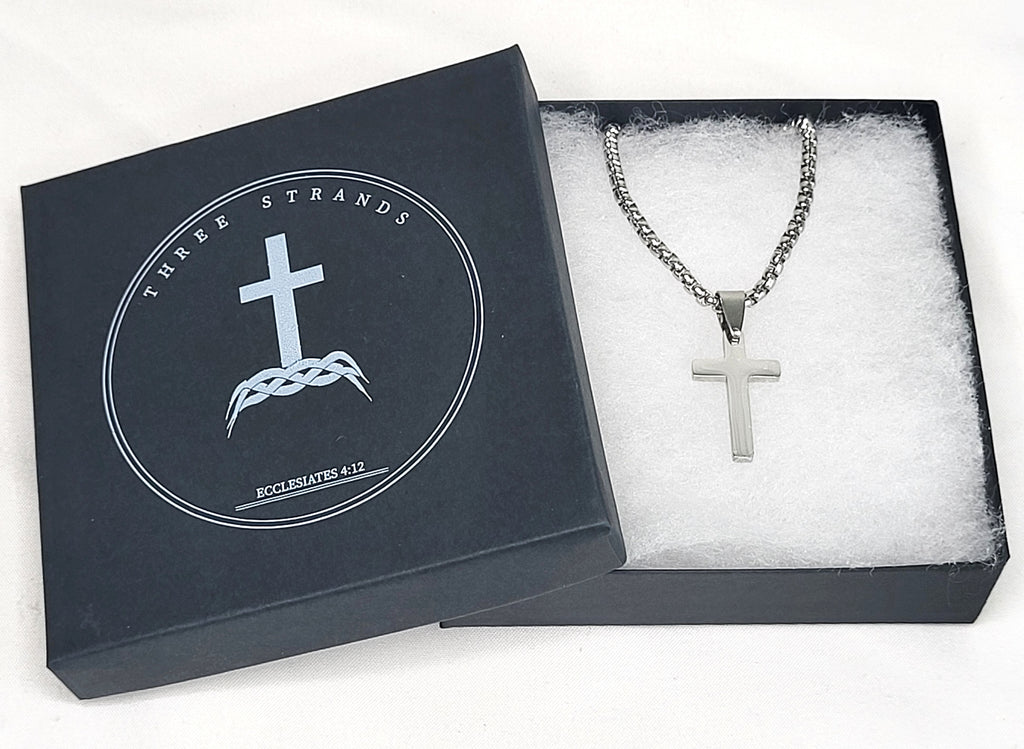Silver cross necklace in a 'Three Strands' branded box on a white background